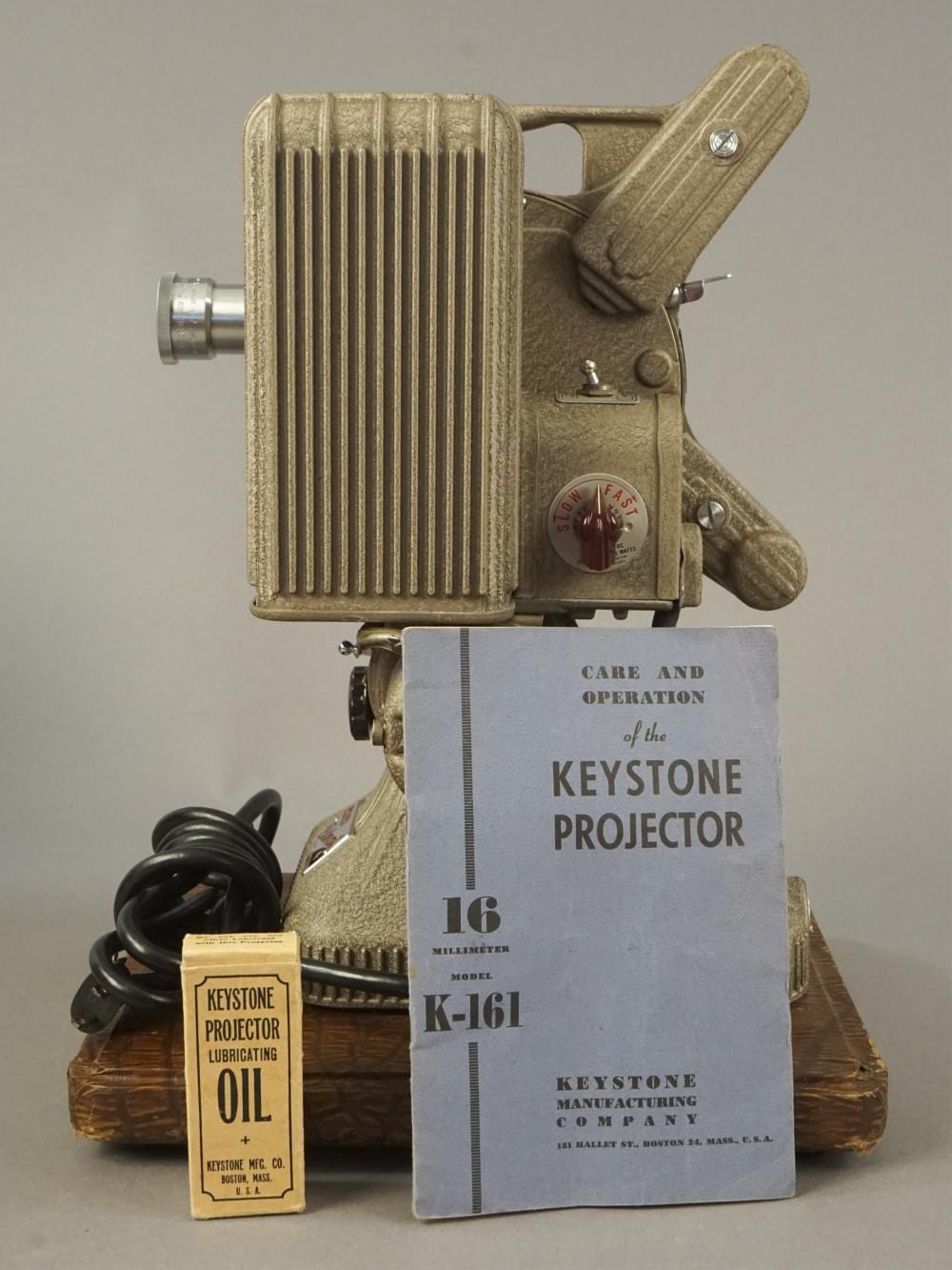 Vintage Keystone 16mm film movie projector with ribbed metal housing and a handle, shown with an instruction booklet and oil bottle.