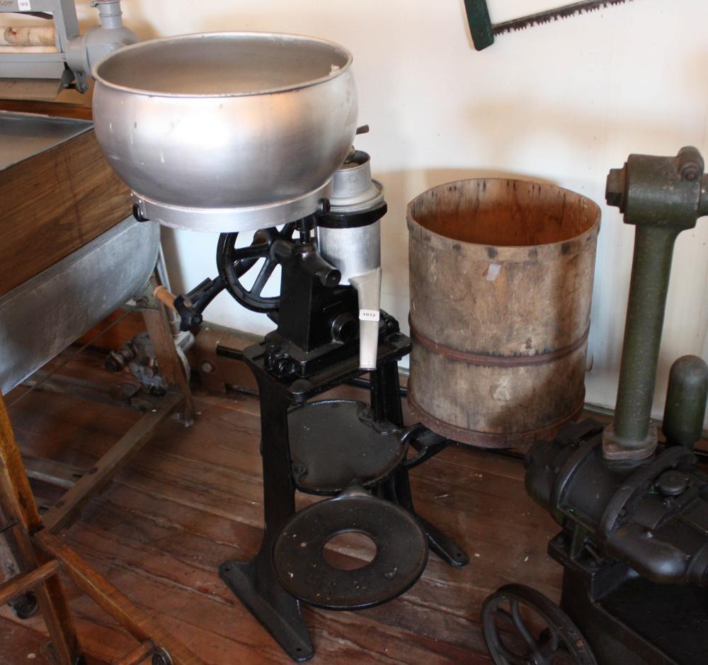 Vintage cast-iron cider press machine with large metal hopper and wooden barrel tank, shown indoors on a wooden floor.