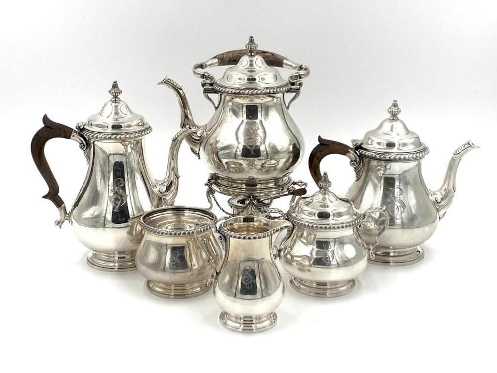 Set of polished silver-colored tea service pieces including a teapot, two teapot-style pots, a sugar bowl, and cream pitcher with ornate finials.