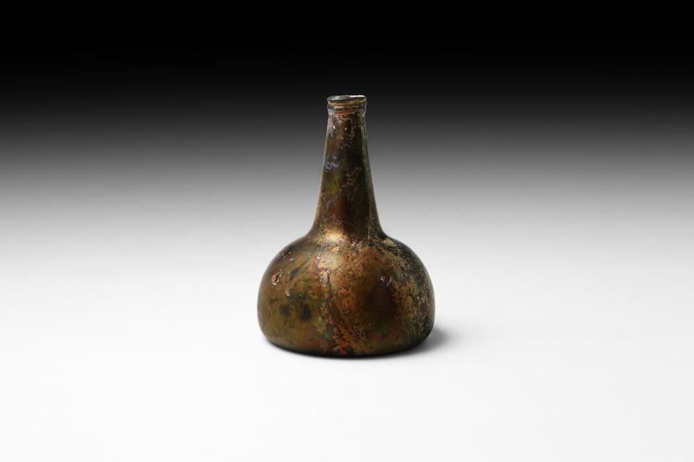 Close-up of an old bronze-colored onion-shaped bottle with a narrow neck and flared rim, on a light background.