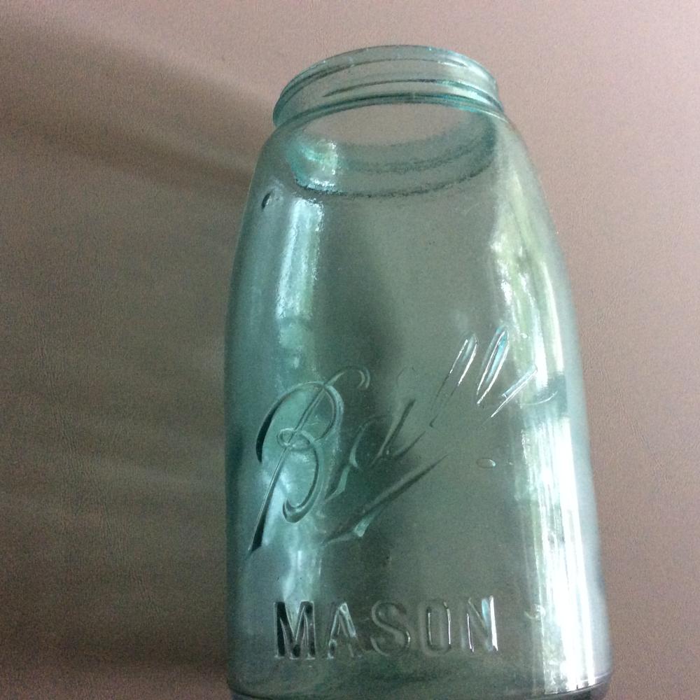 Clear glass ball mason jar with a blue-tinted finish and embossed letters “B” and “MASON.”