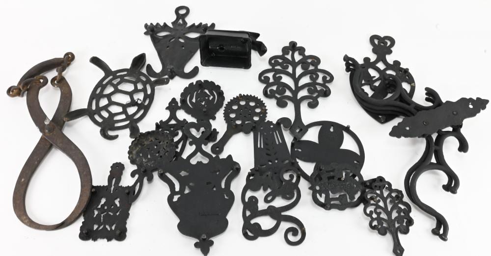 Assorted vintage metal trivet pieces and decorative iron ornaments, including cat and other cutout shapes, on a white background.