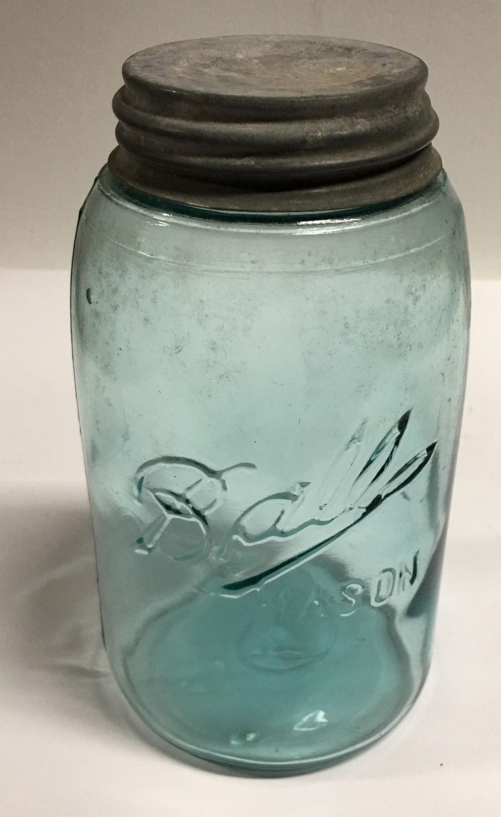 Green glass Ball-style mason jar with a dark lid, decorated with etched flowers and leaves and a partial “Ball” mark near the bottom.