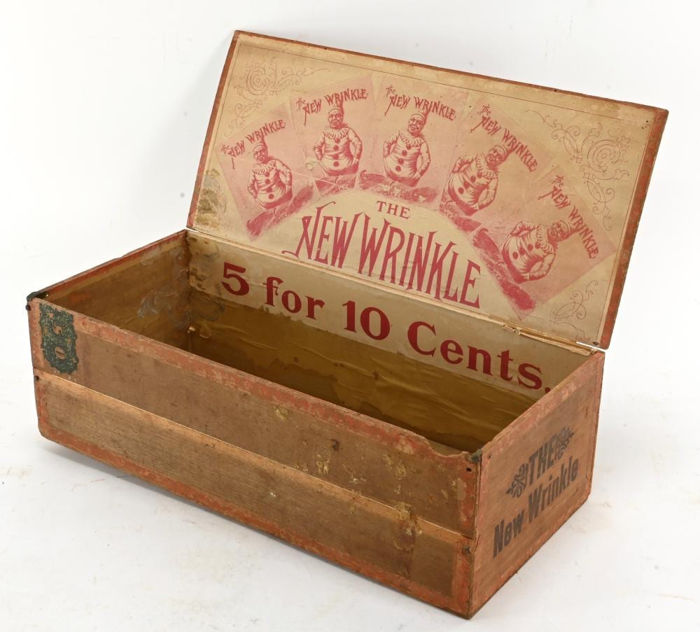 Open wooden cigar box with red printed label reading “THE NEW WRINKLE” and “5 for 10 Cents,” showing clown-like images on the lid.