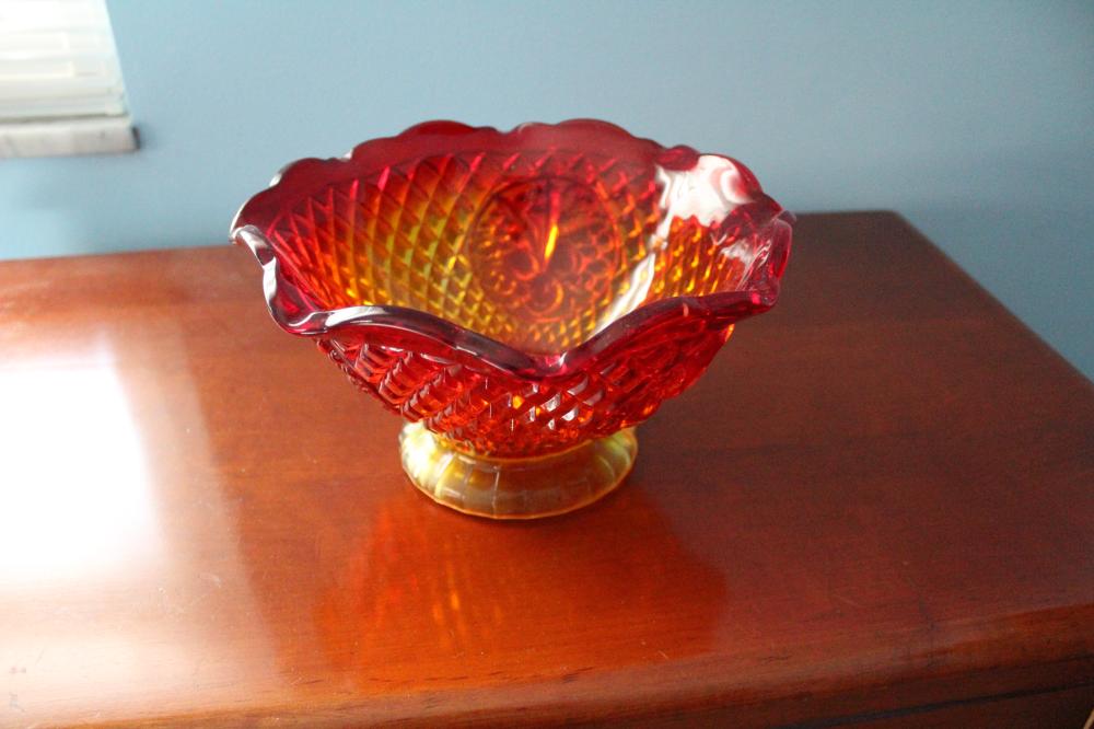 Red, orange, and amber carnival glass bowl with a scalloped rim and diamond fan pattern, photographed on a wooden table.