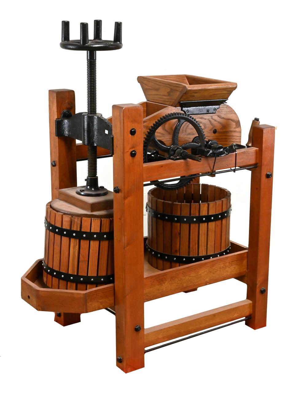 Antique wooden cider press with metal gears and a vertical screw mechanism, mounted on a frame with wooden barrels and straps.