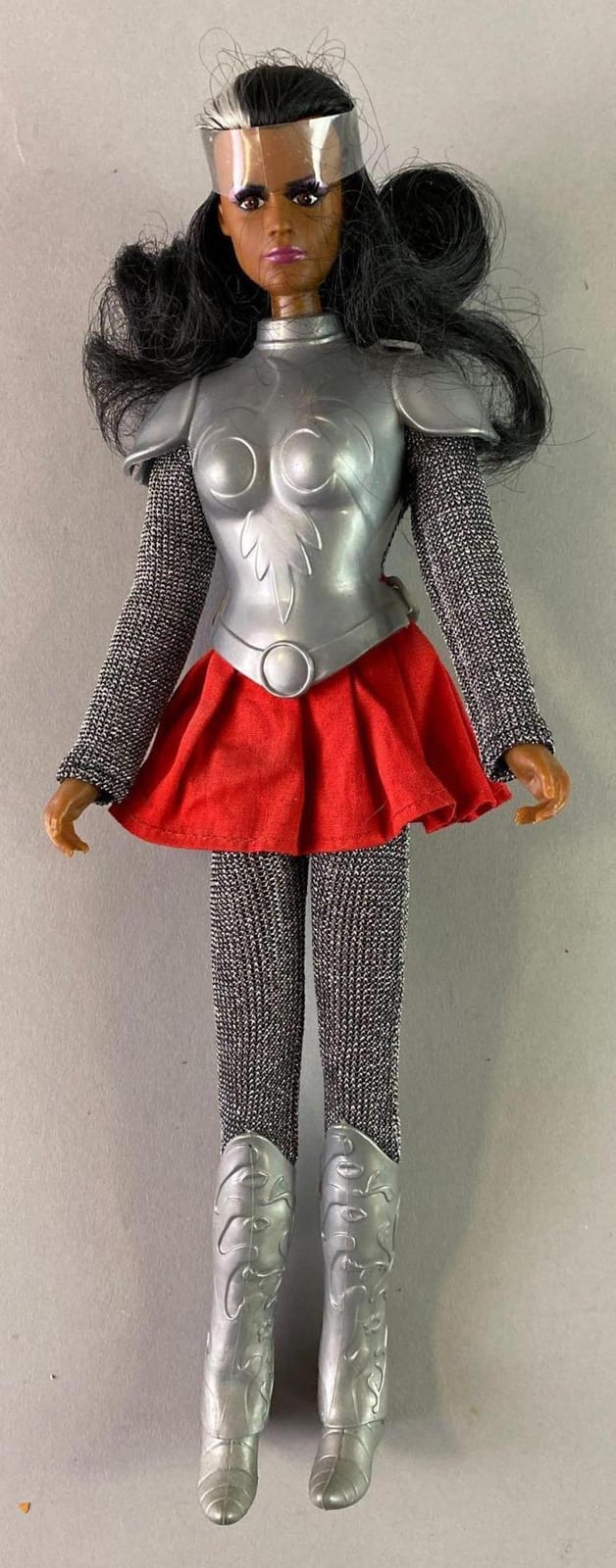 A Wonder Woman–style action figure with silver armored chest, long black wig, red skirt, and mesh-metal sleeves and silver boots.