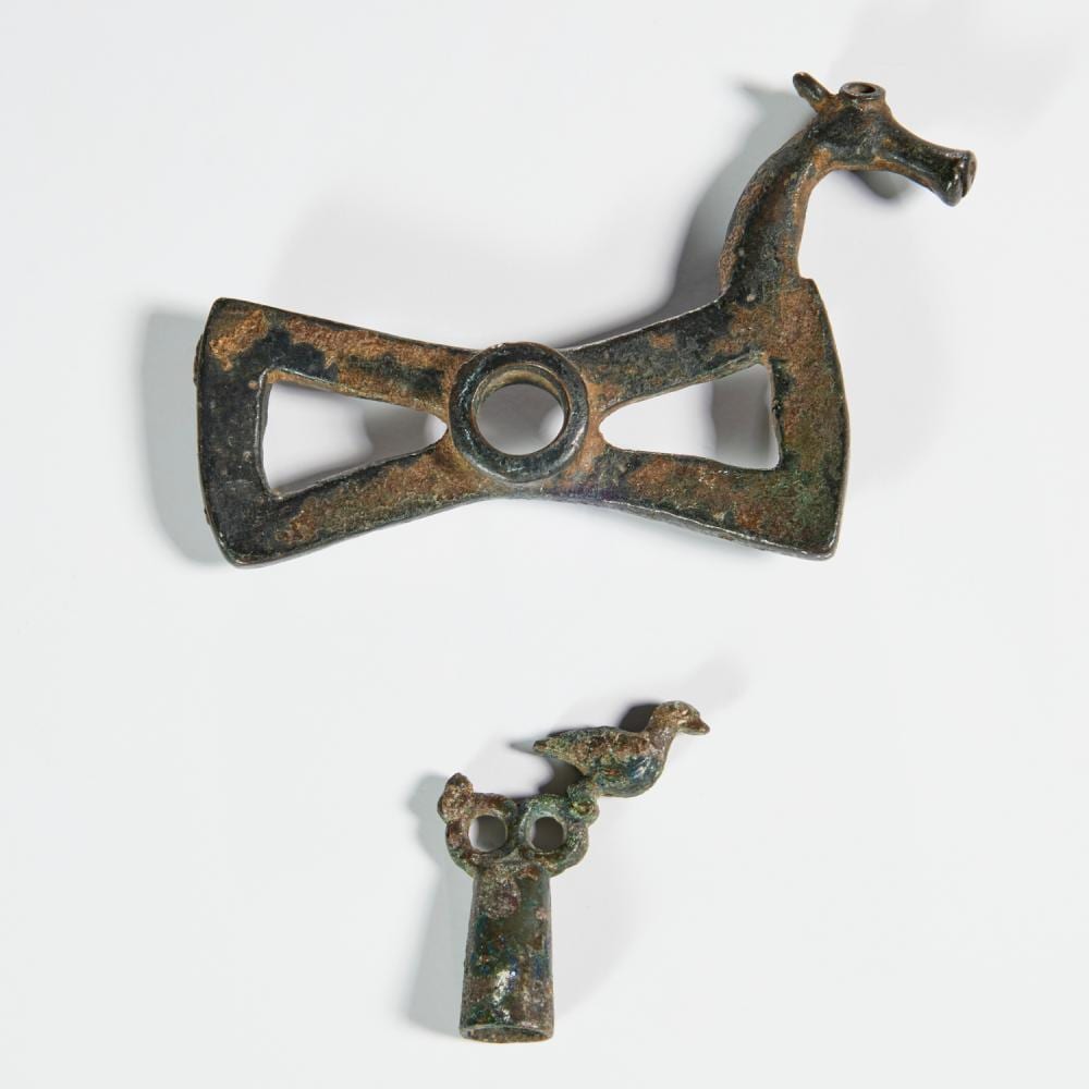 Bronze horse bit with a bow-shaped frame and a small projecting animal head, shown against a white background.