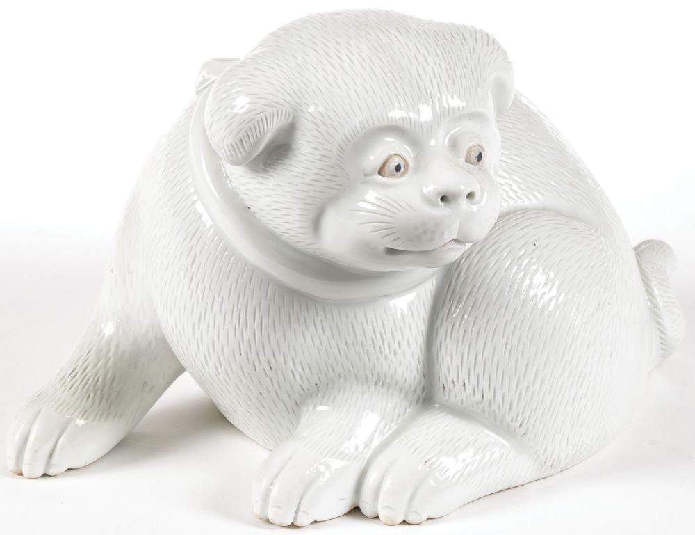 White ceramic figurine of a crouching dog with textured fur pattern and small raised ears, shown against a white background.