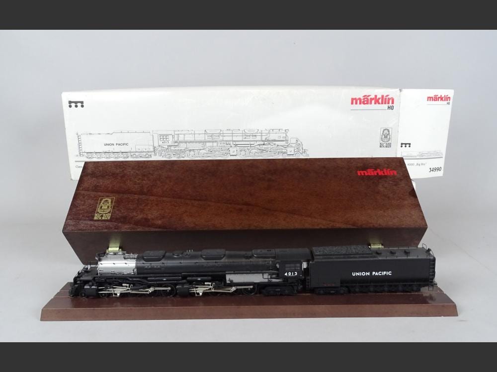 Model steam locomotive in dark gray with “Union Pacific” lettering, set in a brown wooden presentation box; Märklin HO packaging in the background.
