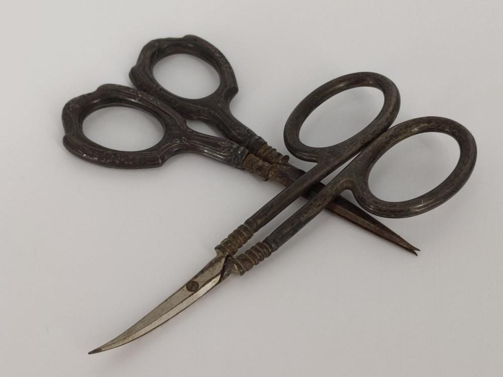 Two small embroidery scissors with arched finger loops and pointed blades, shown together on a light background.