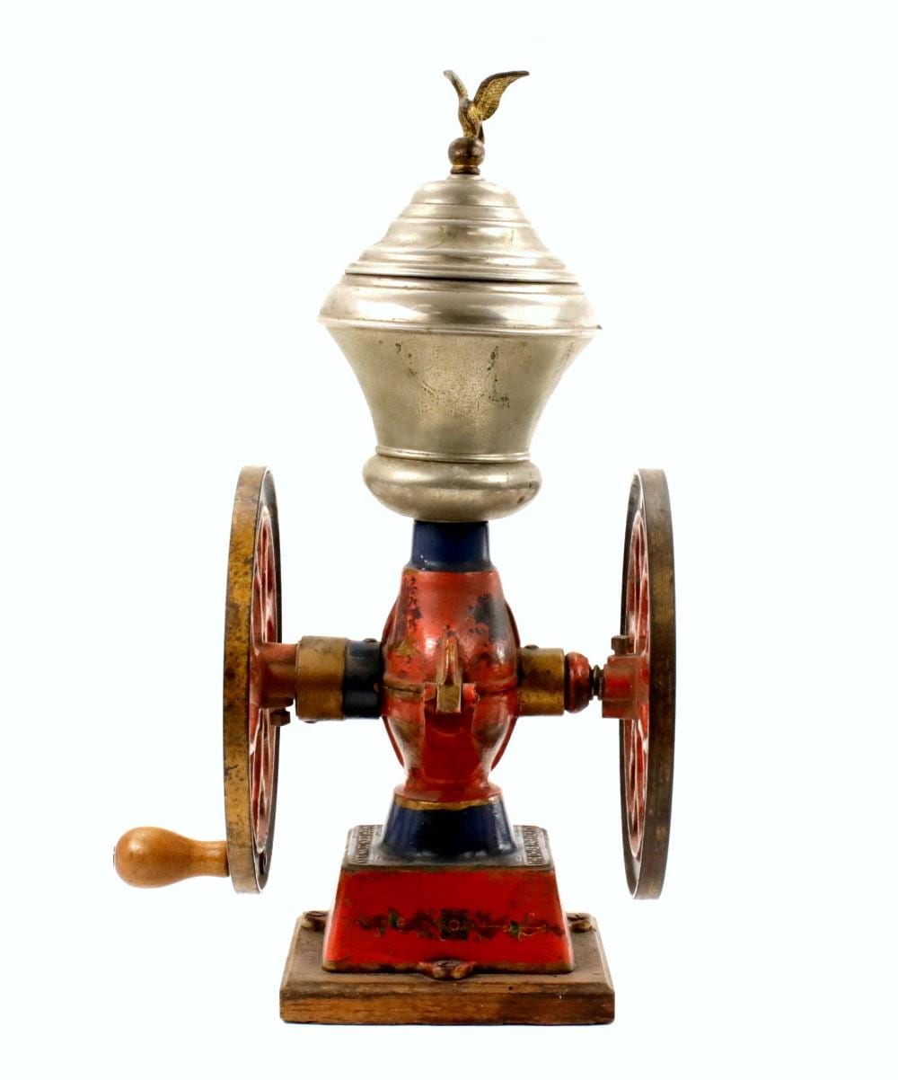 Antique-style metal coffee grinder with a finial knob on top, mounted on a wooden base with two side wheels and a crank handle.