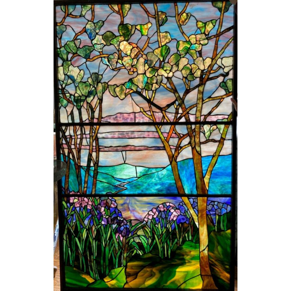 Colorful stained glass window panel with trees, green foliage, flowers, and a blue sky over a river or path.