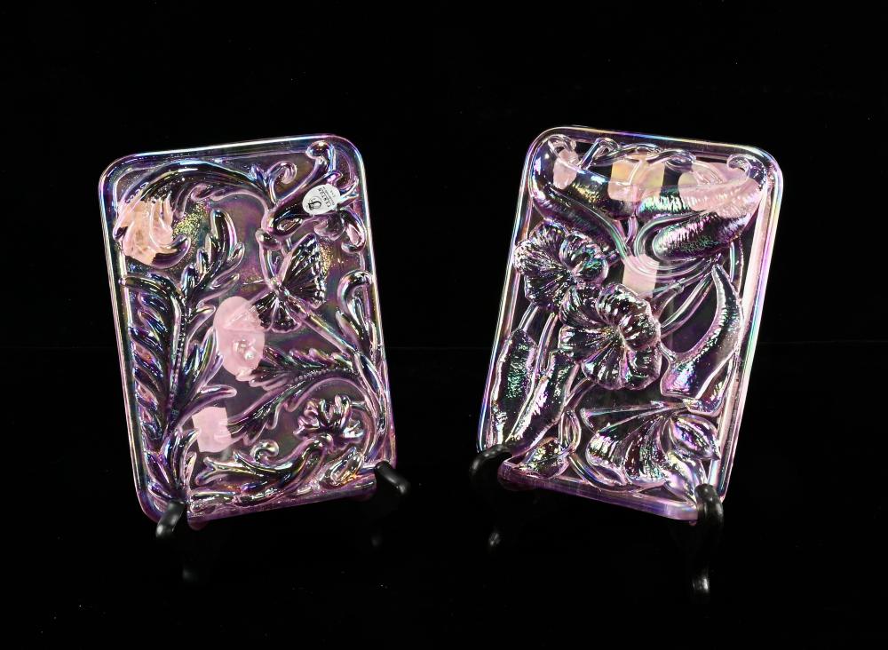 Two purple, iridescent glass decorative plaques with raised floral and leaf patterns on dark stands.