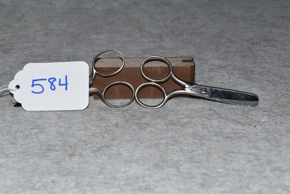 Pair of small metal scissors with circular finger rings and two blades, shown on a gray surface.