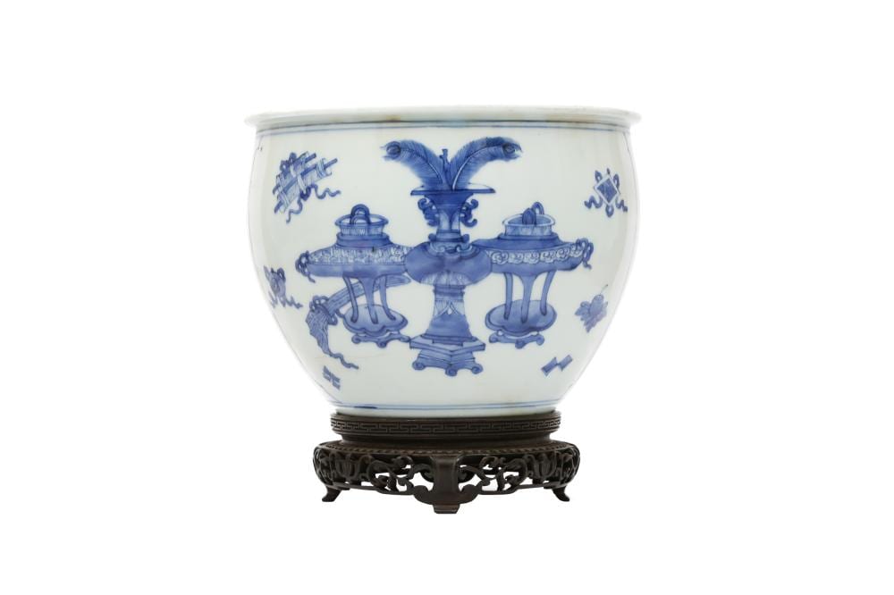 Chinese blue-and-white porcelain fishbowl with blue decorative floral and scroll motifs, shown on a dark carved stand.