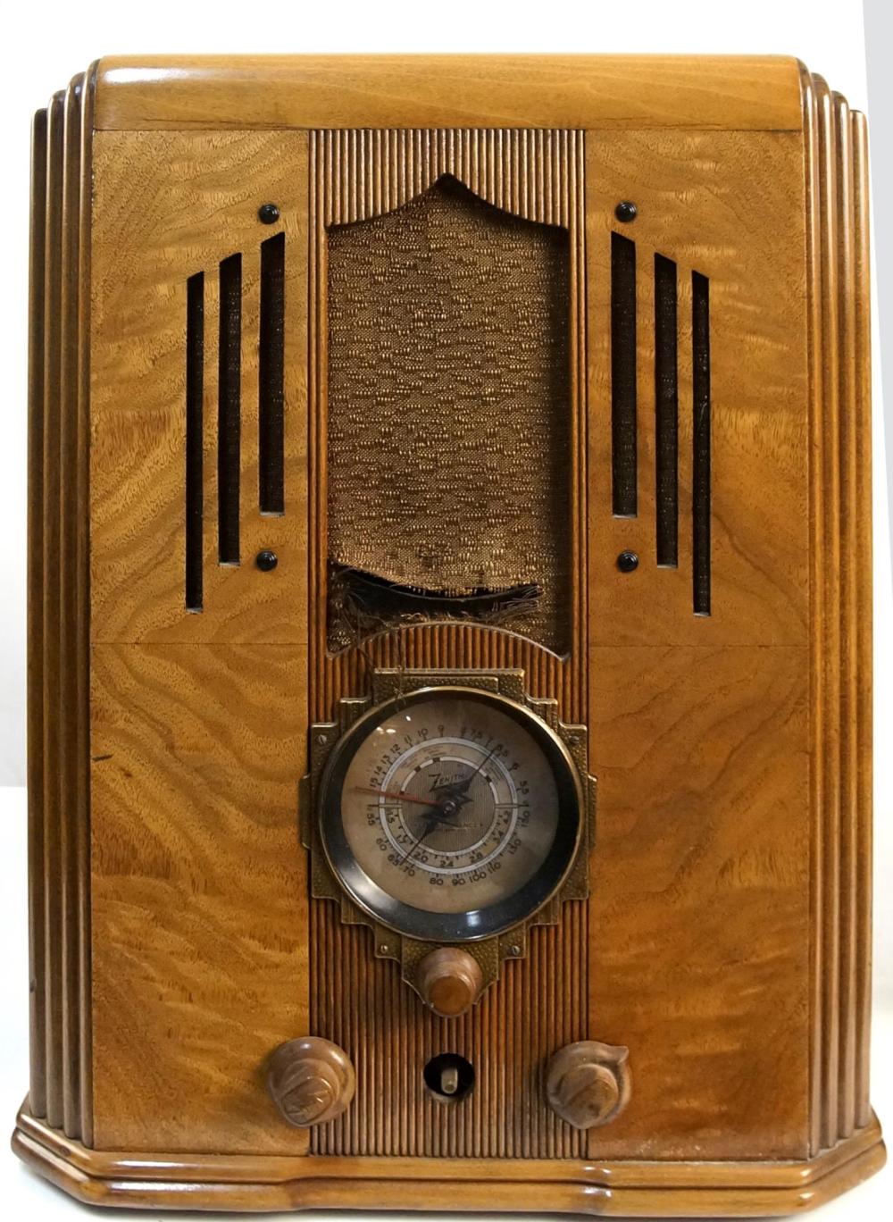 Vintage wooden tombstone-style tube radio with a gold-toned front panel, grill speaker area, vertical grille slots, and a round tuning dial labeled “Zenith.”