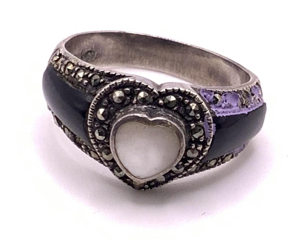 Close-up of a vintage-style sterling silver ring with dark enamel and small rhinestone-like stones, featuring a heart-shaped center.