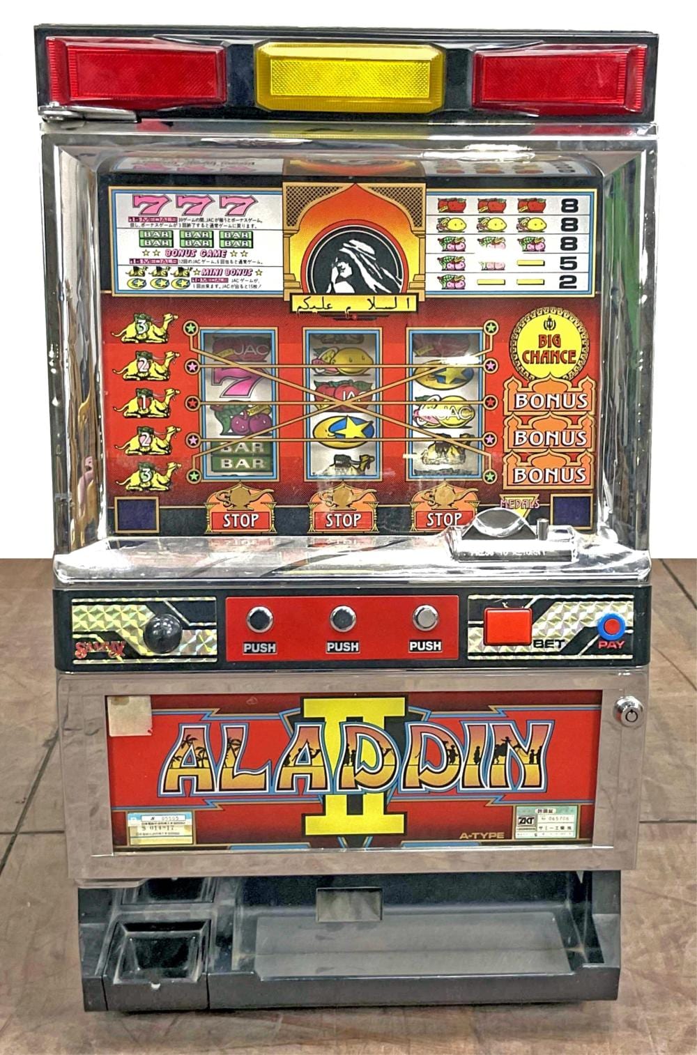 Front view of a slot machine with a colorful triple-reel game screen and buttons labeled PUSH, STOP, and BET/PAY; banner reads “ALADDIN II.”