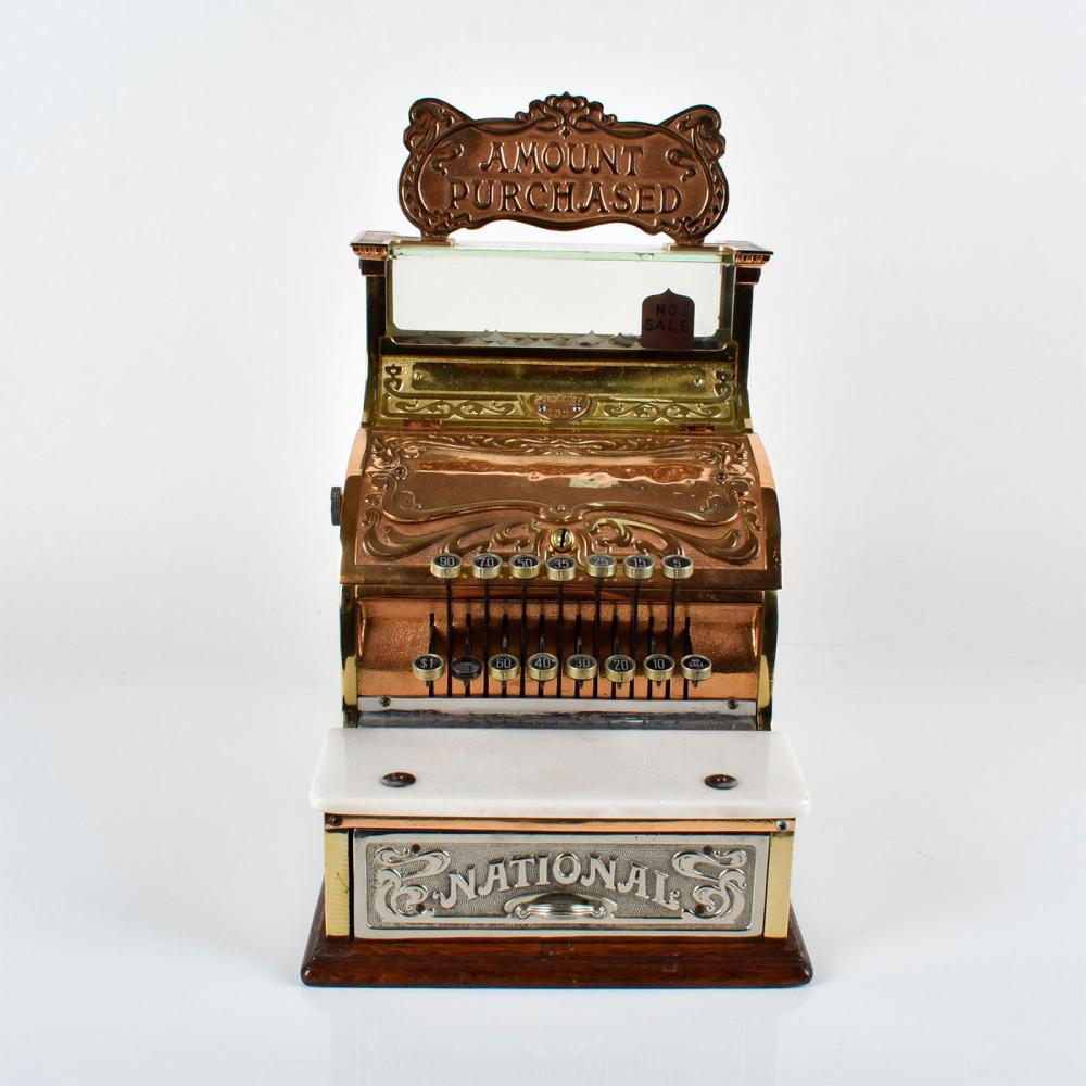 Antique-style brass cash register with ornate scrollwork, an “AMOUNT PURCHASED” panel, and coin and number dials.