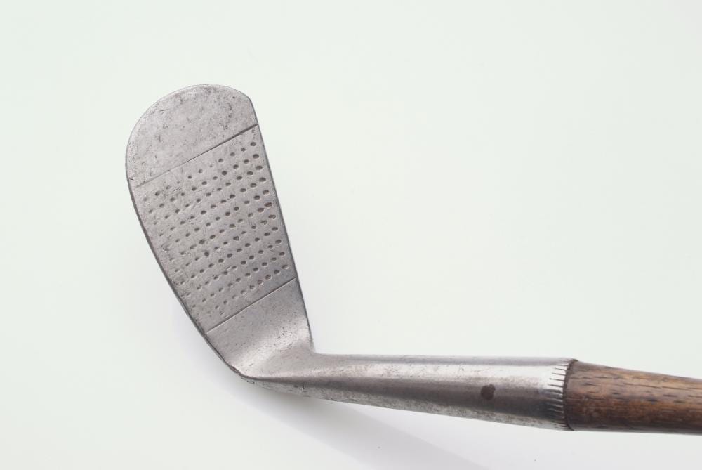Close-up of a golf club head with a perforated striking face and a wooden handle on a white background.