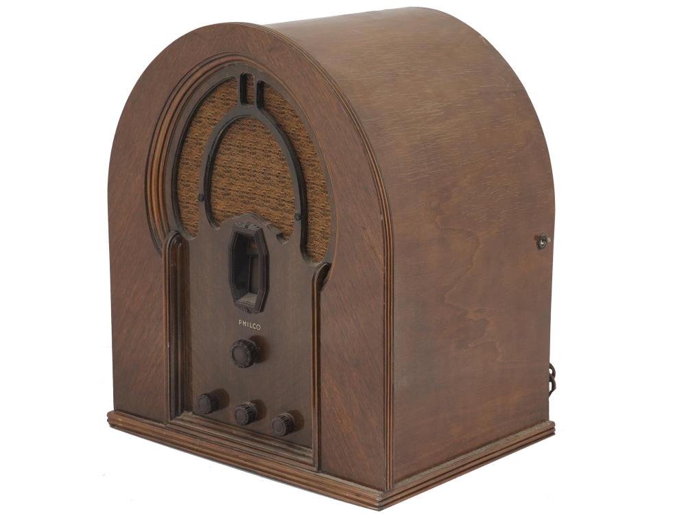 Vintage wooden tabletop radio with arched front panel, speaker grille, and analog tuning knobs labeled “PHILCO”.
