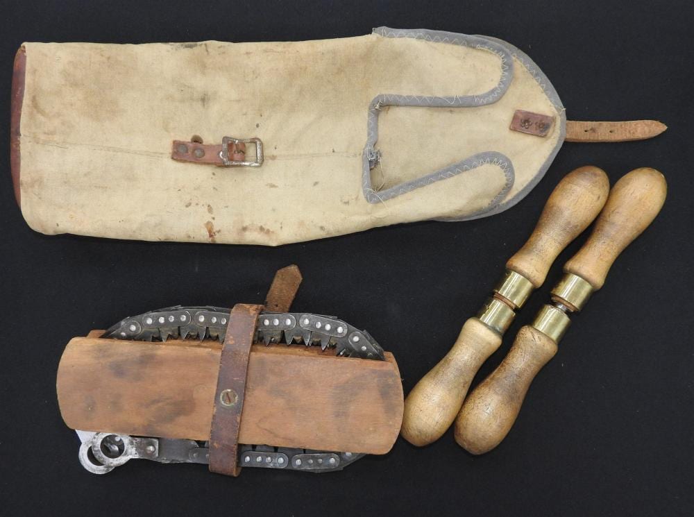 Antique crosscut saw tool with wooden handles, metal blade, and scabbard-like sheath laid on a dark background.