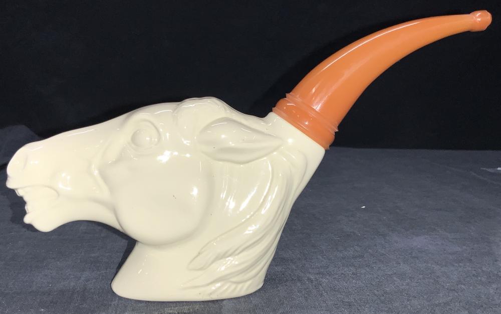 White ceramic pipe-shaped cologne bottle with an orange curved spout, photographed against a dark background.