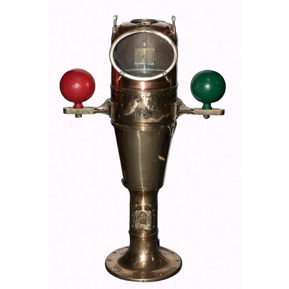 Brass marine binnacle with a circular compass dome and two colored hand knobs, shown front view on a round base.