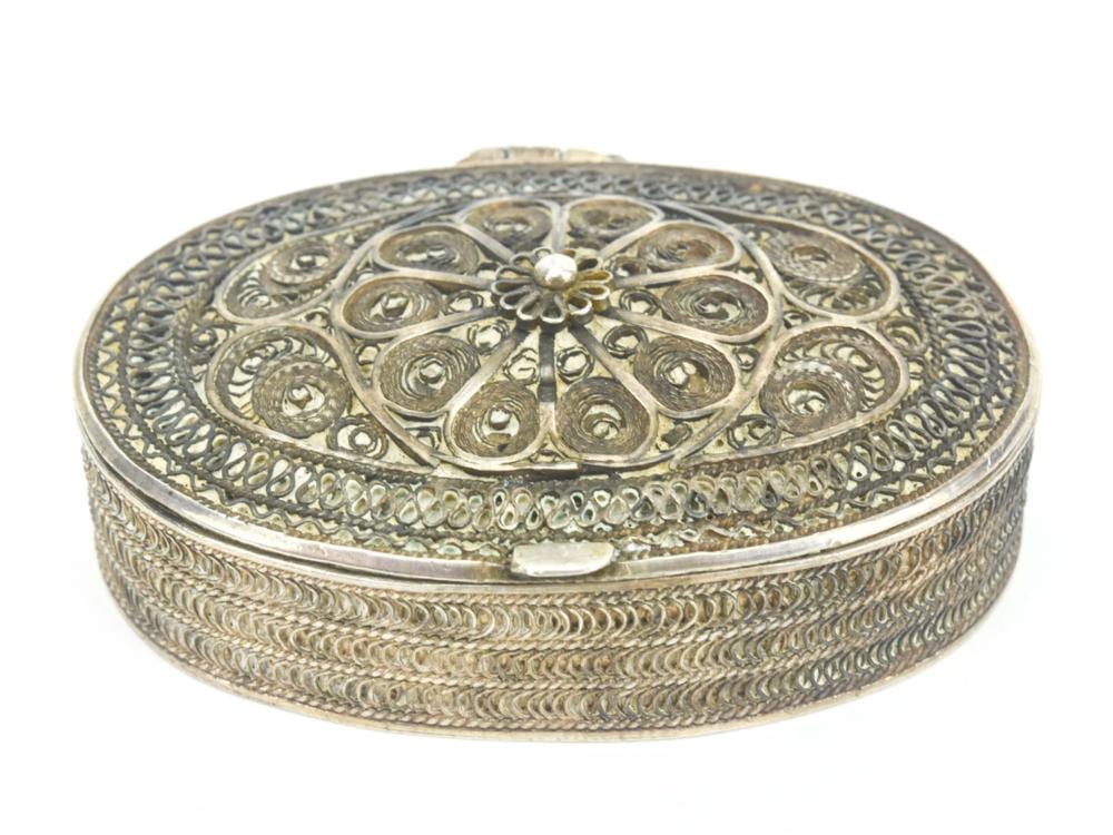Close-up of an ornate oval metal pill box with embossed decorative band and floral-style medallion on top.