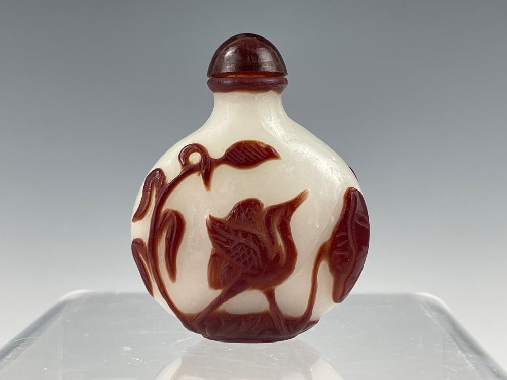 Small rounded glass snuff bottle with dark red spiral-and-bird relief design and a red stopper on top.