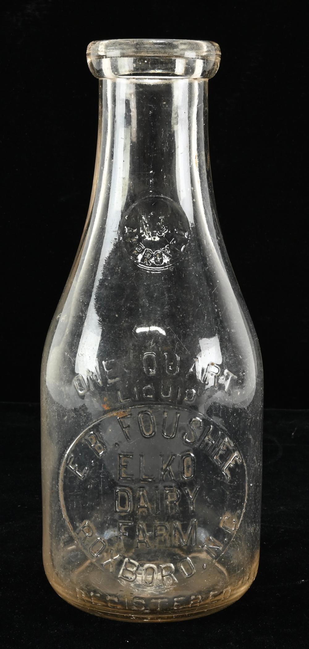 Clear glass milk bottle with embossed lettering near the base reading “E. B. Foushee,” on a dark background.