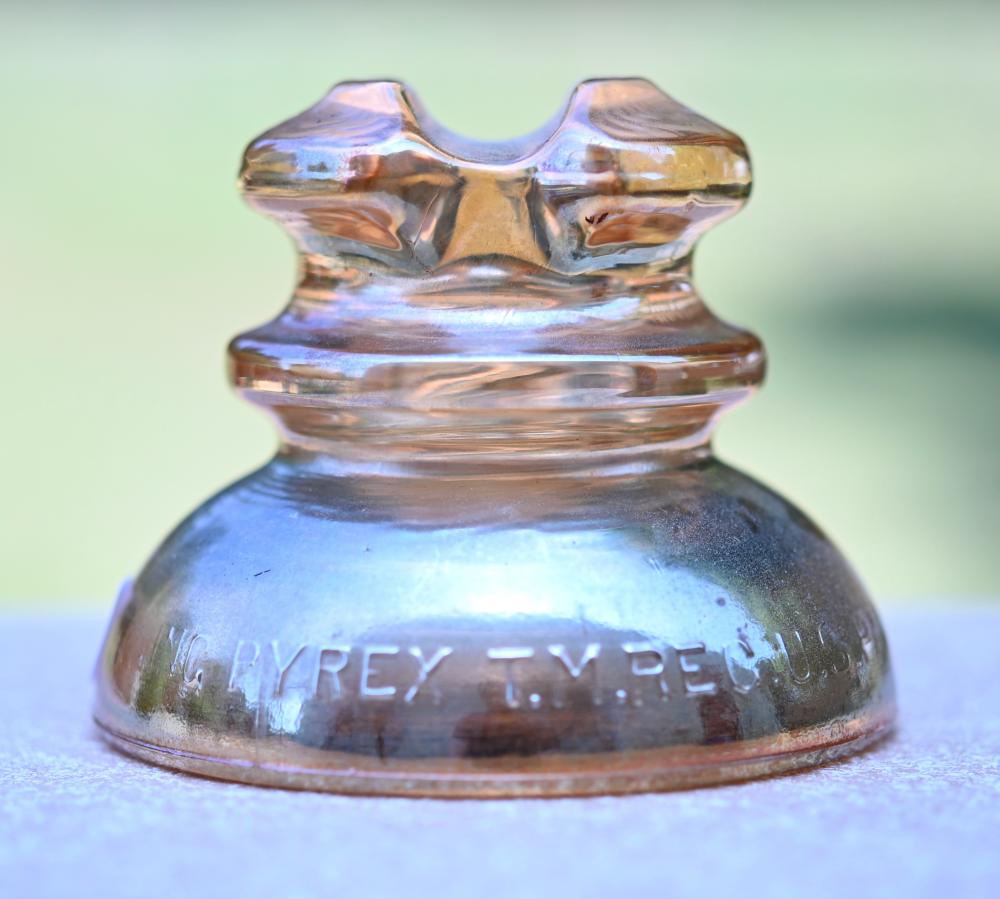 Vintage glass insulator with a fluted crown top and glossy iridescent finish, stamped with the words “PYREX-TYPES”.