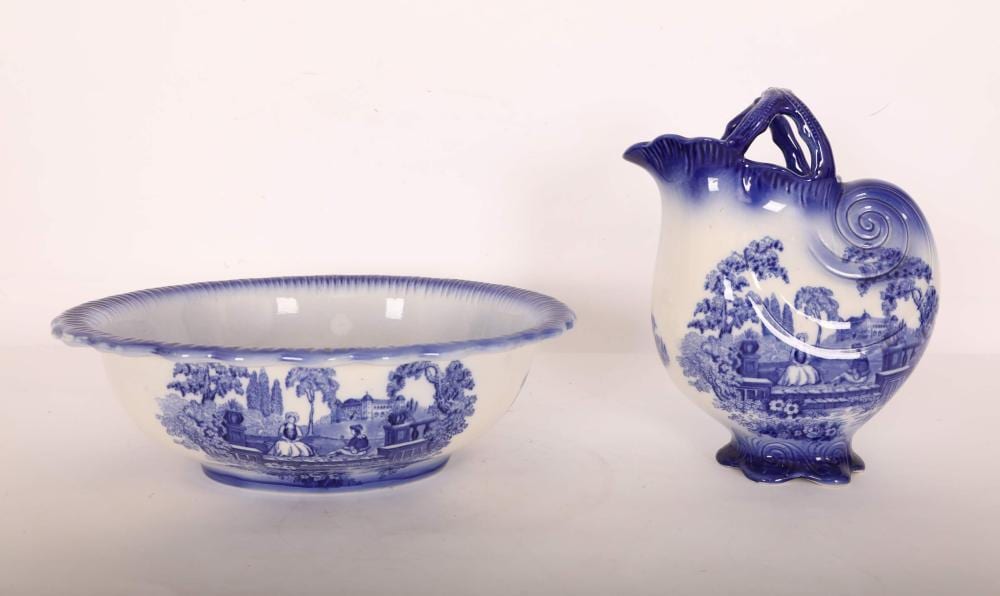Blue-and-white ceramic wash basin and shell-shaped pitcher with landscape scenes on a light background.