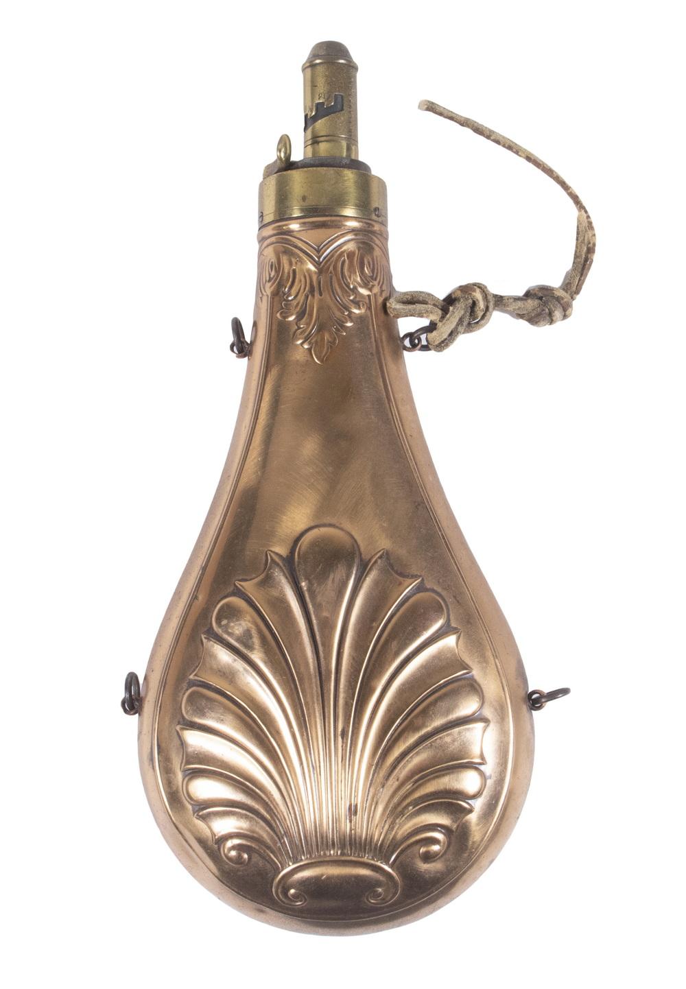 Brass-toned powder flask with embossed floral ornament, hinged spout, and a metal wire handle on a white background.