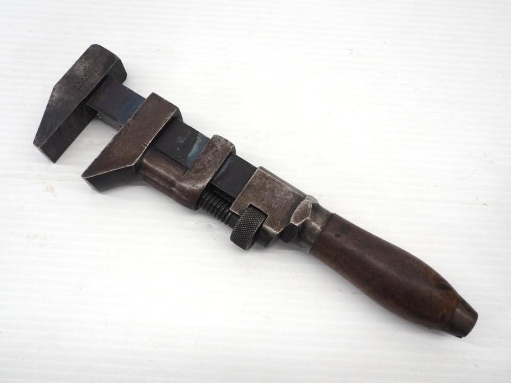 Metal adjustable wrench with open jaws and knurled adjustment wheel on a plain light background.