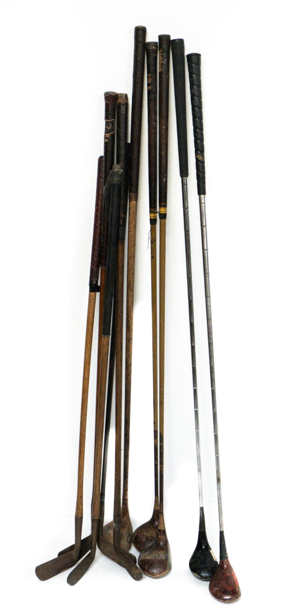 Group of vintage golf clubs and golf iron heads standing upright on a white background, showing multiple shafts and club heads.