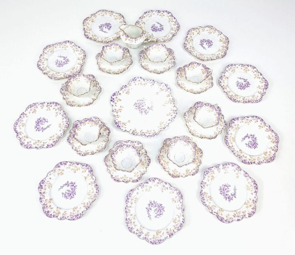 Assortment of decorative white bone china cups and saucers with purple floral center and scalloped, gilded edges.