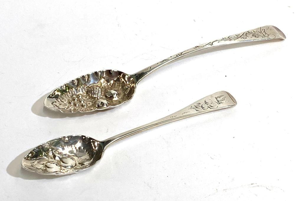 Two ornate metal berry spoons on a white background, each with a patterned oval bowl and engraved handle.
