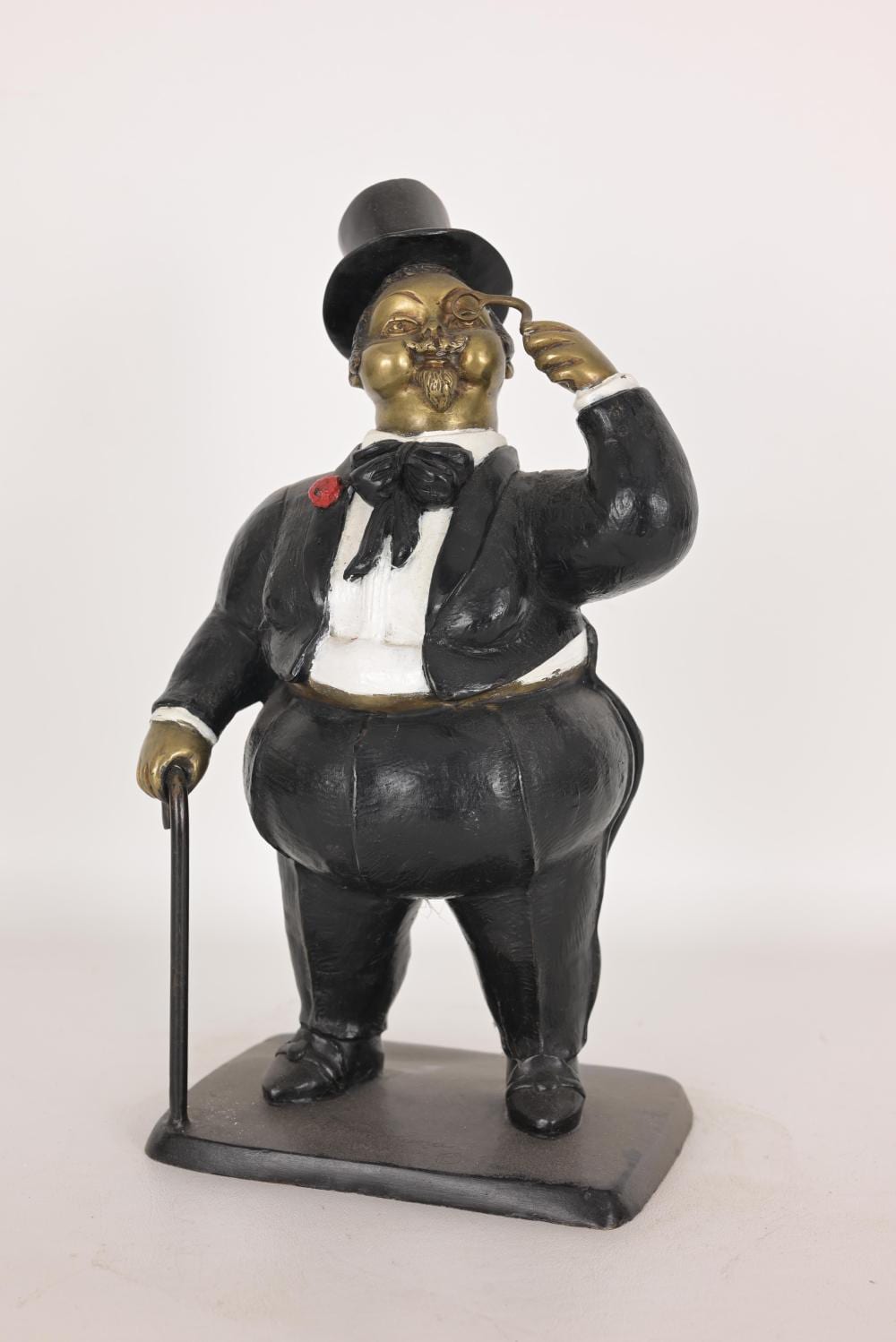 Bronze sculpture of a suited man with a top hat, holding a cane and tipping his head to one side.