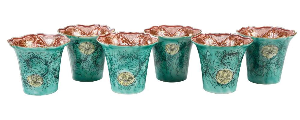 Set of six turquoise ceramic sake cups with painted floral and wave-like designs and red patterned rims, shown side by side.