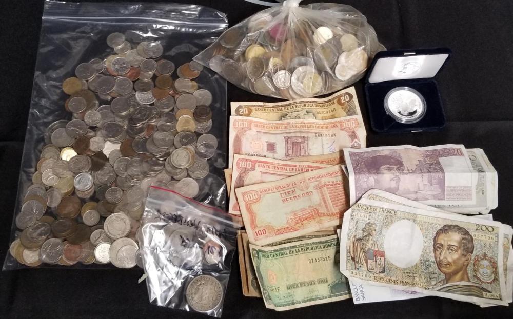 Bagged mixed coins and banknotes, including a coin in a black presentation case and several bills laid on a dark surface.