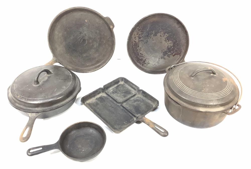 Group of gray cast-iron cookware pieces including two skillets, two round lids, a square griddle, and a small skillet pan.