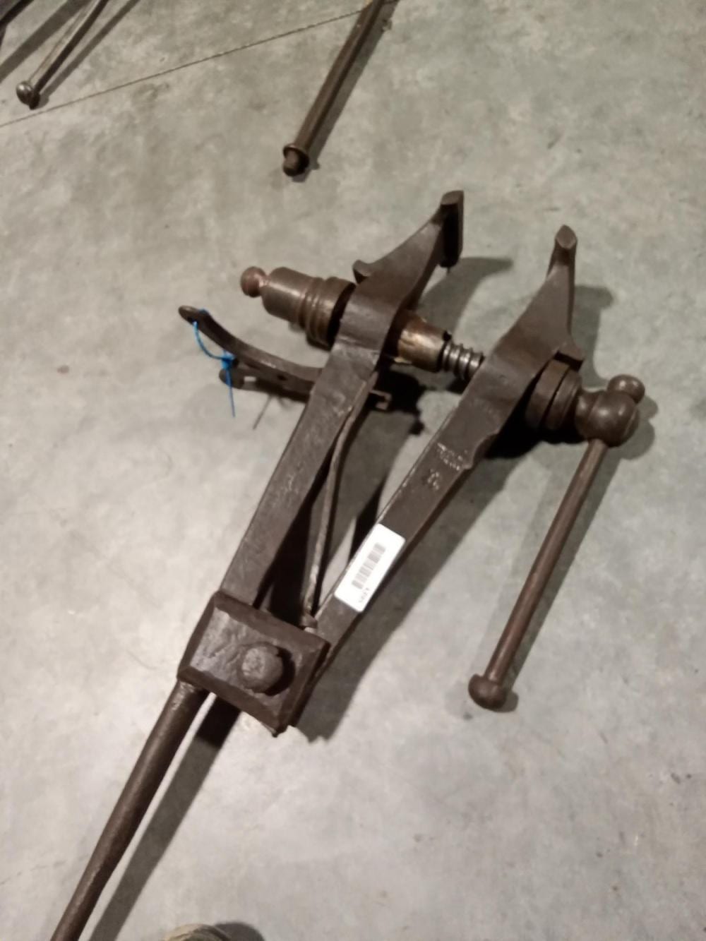 Metal post vise tool with a screw mechanism and jaws, shown angled on a concrete floor.