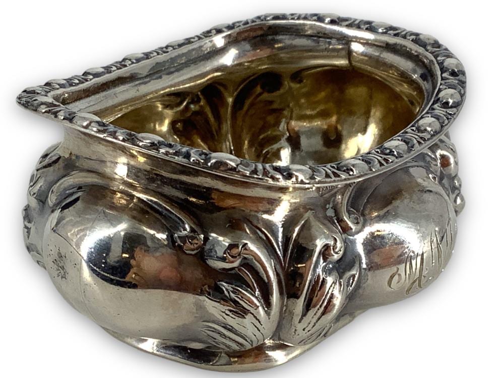 Shiny silver-toned salt cellar with an open top and ornate raised border, viewed from above at an angle.