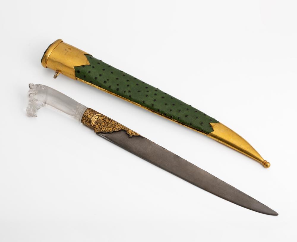 Two antique dagger-like blades with dark green patterned grips and gold-colored hilts, shown on a white background.