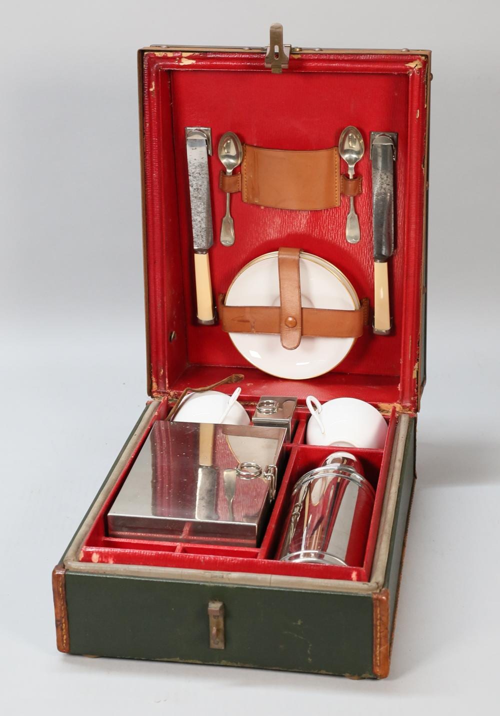 Open vintage-style picnic basket set with red interior lining, silver cutlery, and white plates.
