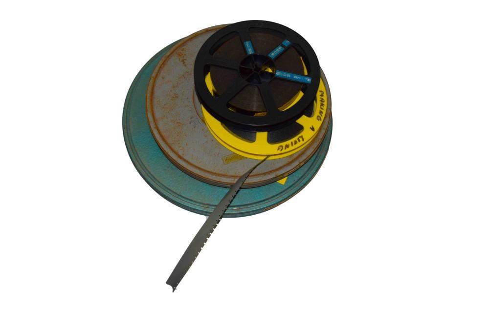 Spool of 16mm film with dark reels and yellow label, shown on a round metal can with part of the film leader extending.