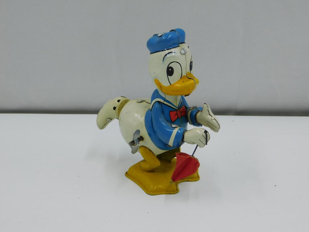 Wind-up tin lithograph style Donald Duck figure in a blue sailor outfit, holding an arm out and a red bucket-like accessory in front.