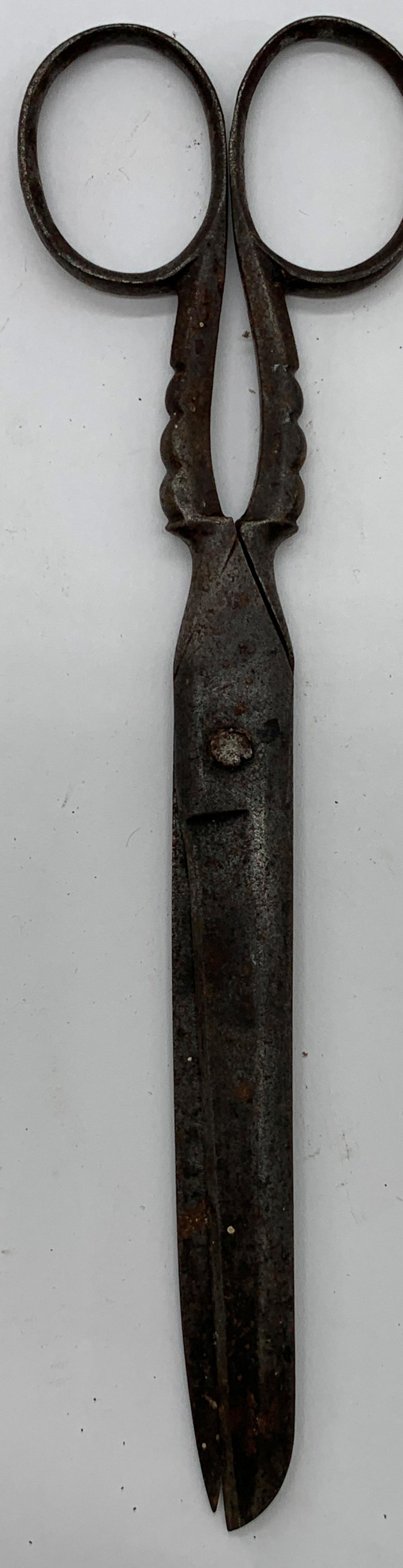 Antique-looking metal scissors shown from above with closed blades and loop handles, photographed against a white background.